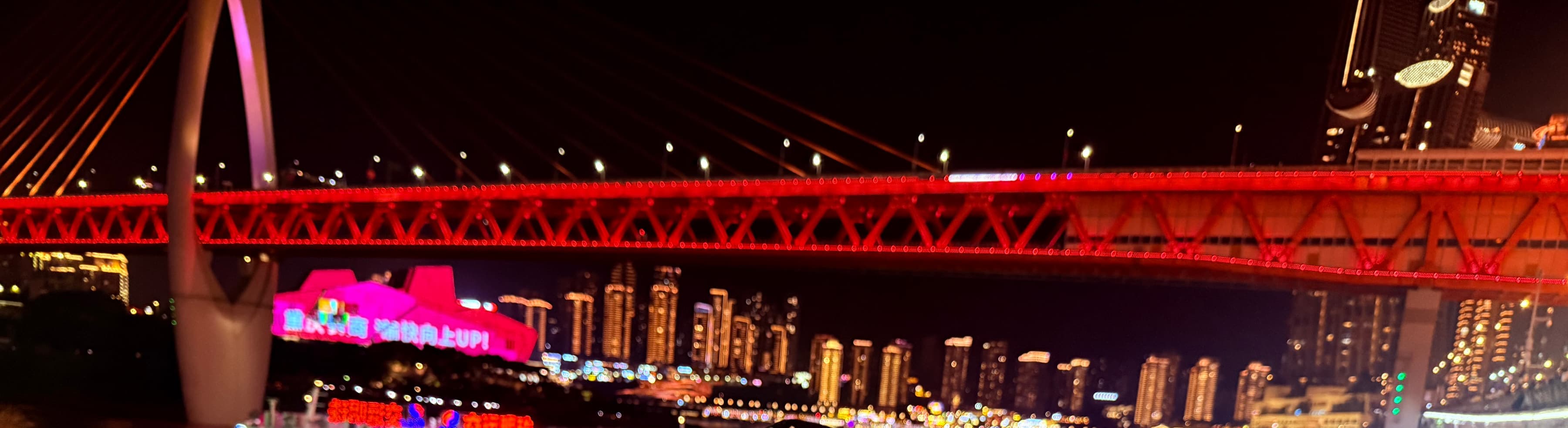 Chongqing at night: a red-lit bridge over the river and the skyline beyond