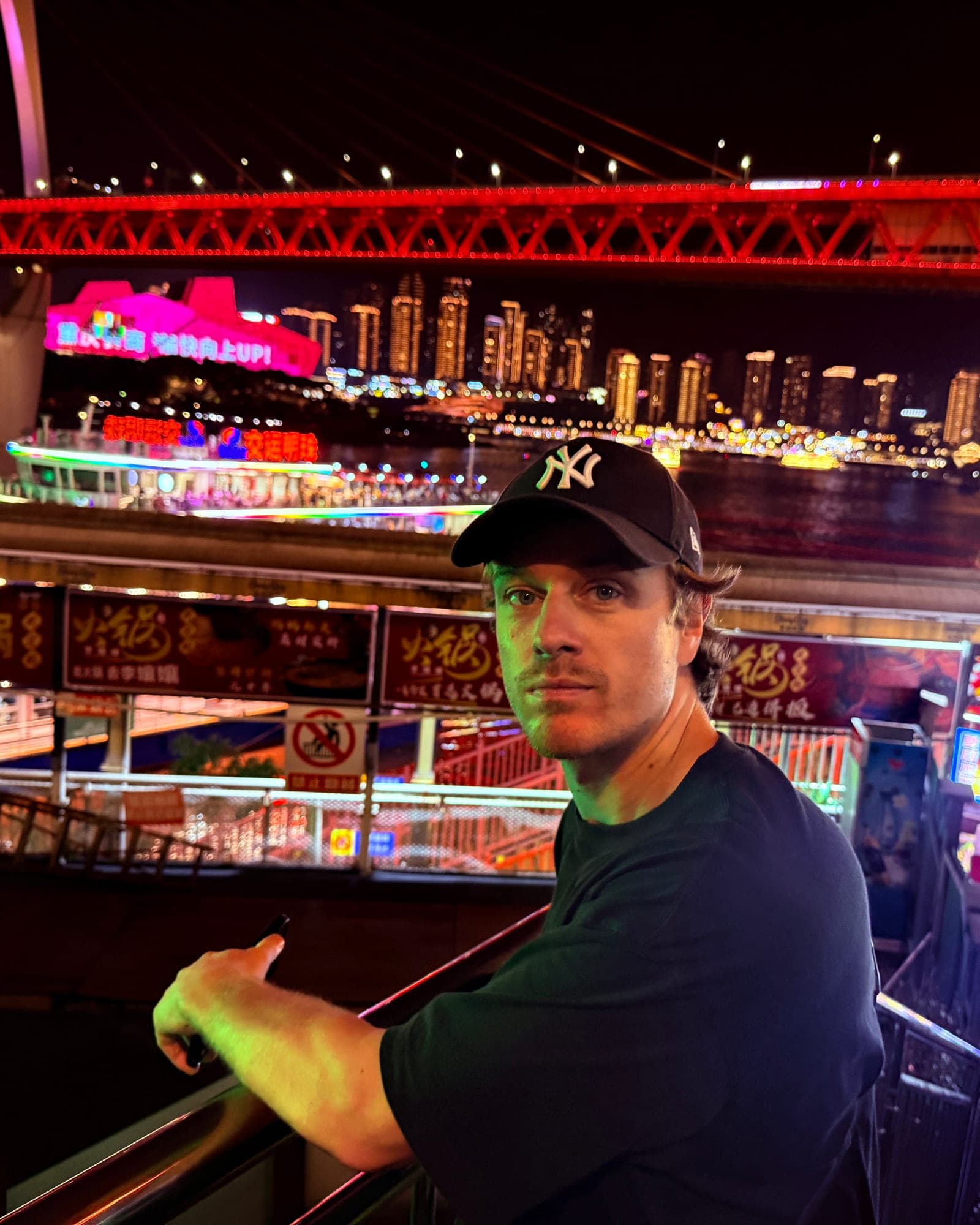 Jorn Bouwmeester at night by the river in Chongqing, neon signs and a lit bridge behind him